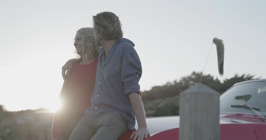 A man has his arm around a woman as they sit on a car