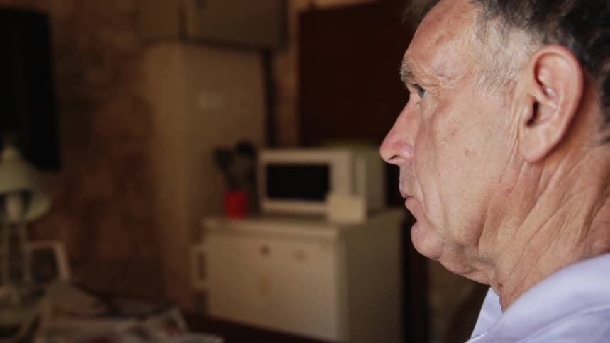 An older man is sitting in thought inside his home in daylight