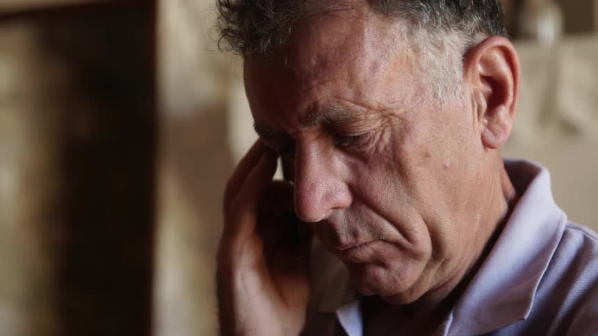 A man leans forward rubbing his head
