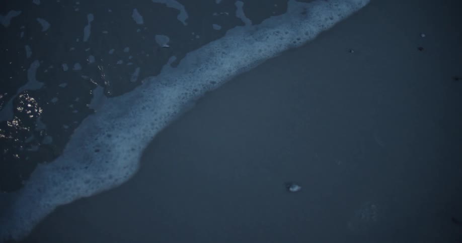 A wave is lapping the sand on a beach at dusk