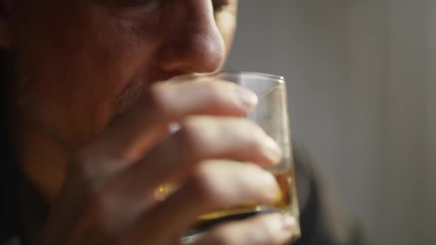 The man looks at a ring, and takes a drink