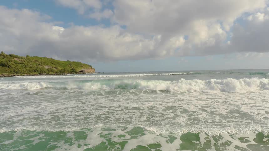 Waves are rolling and crashing towards a beach on a cloudy day