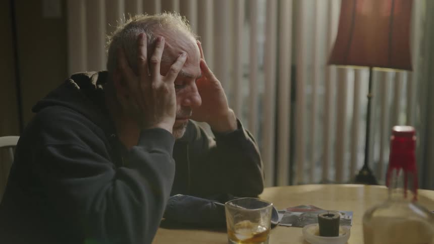 Depressed looking man sitting at a table holding his head
