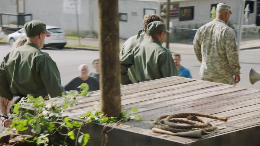 A group of soldiers are leading two prisoners while a crowd watches during the day
