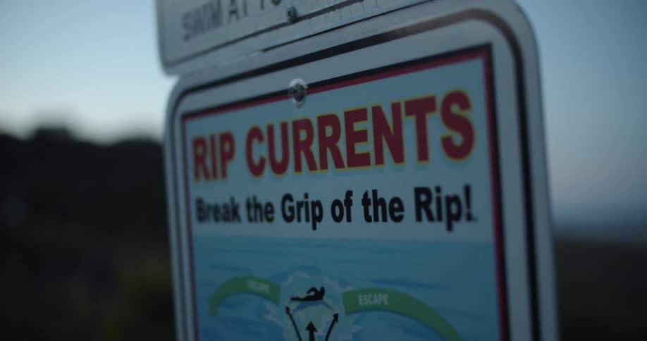 A sign warning of rip currents stands on a beach