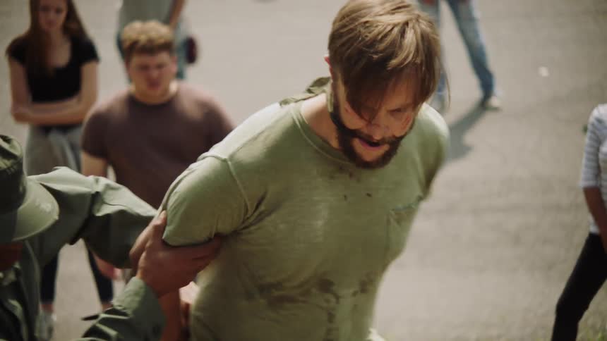People watch as a bound and gagged man is pulled away by a military person