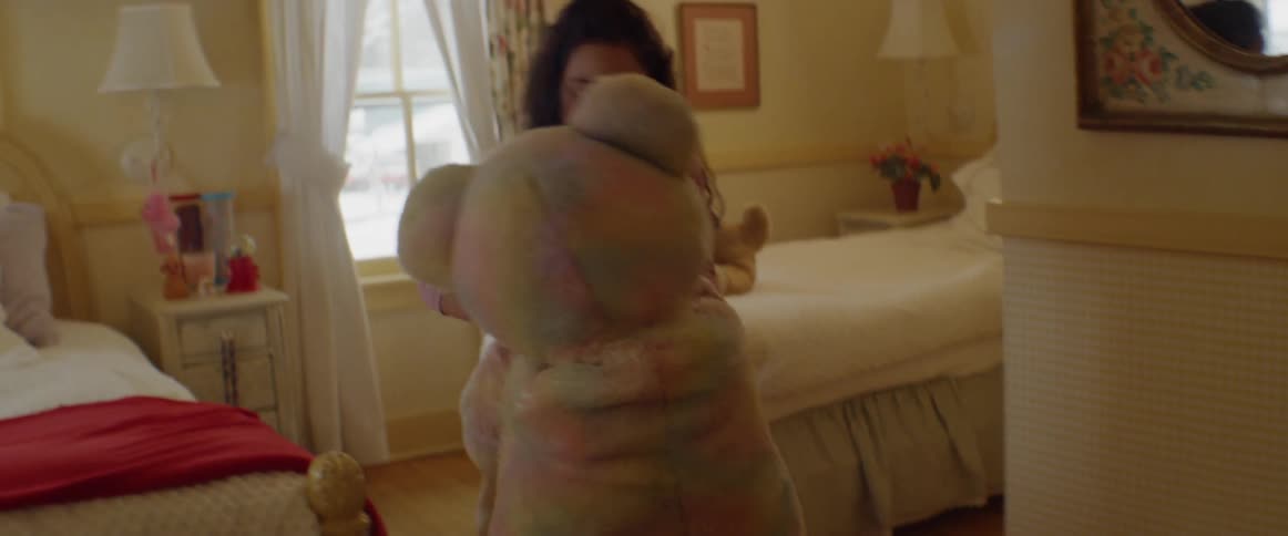 A girl dances with a large teddy bear in her bedroom