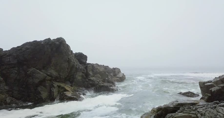 The heavy waves crash against the foggy shore