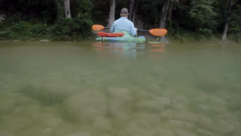 A man is paddling a kayak on a river in daylight
