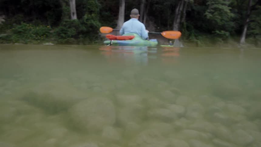 A man is paddling a kayak on a river in daylight