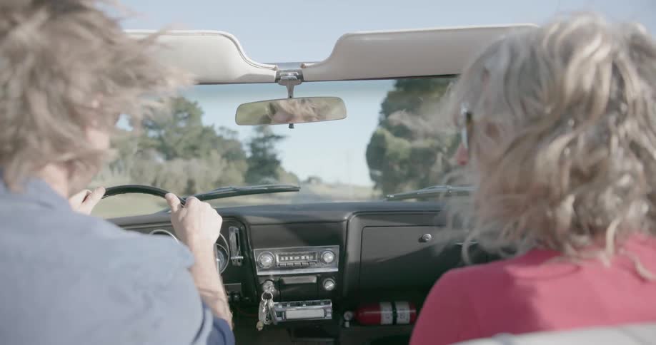 A man and woman smile as they ride in a convertible