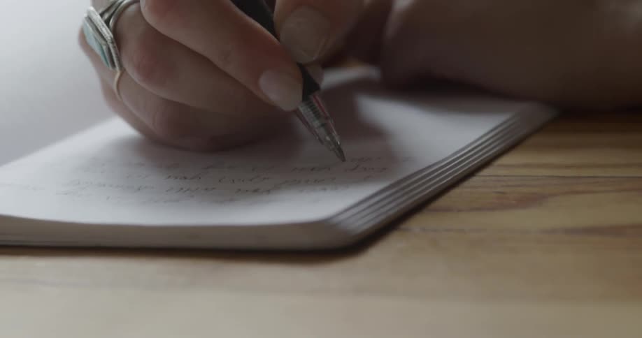 Person writes in a notebook at a table