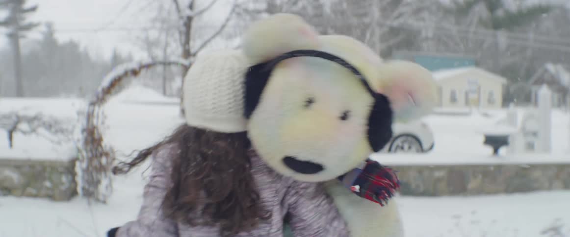A girl carries a teddy bear in the snow