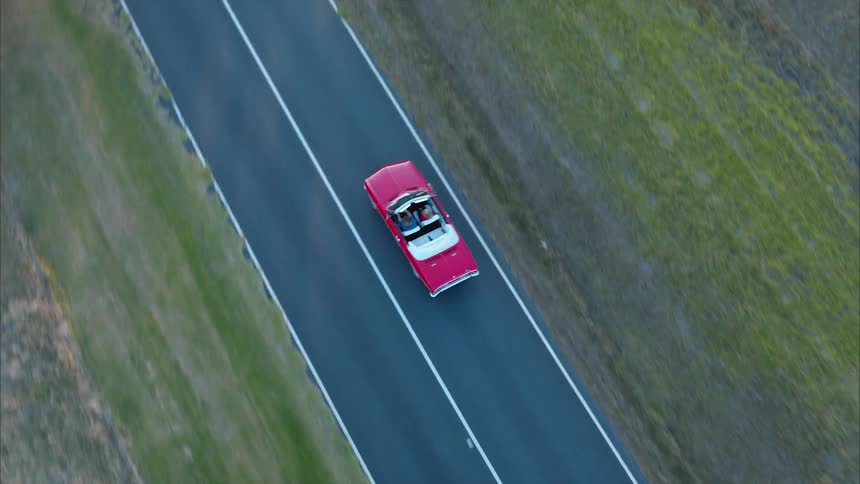 A red convertible travels on a rural road on a sunny day