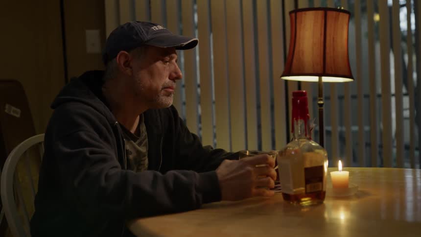 Man sits at table drinking whiskey and looking at pictures