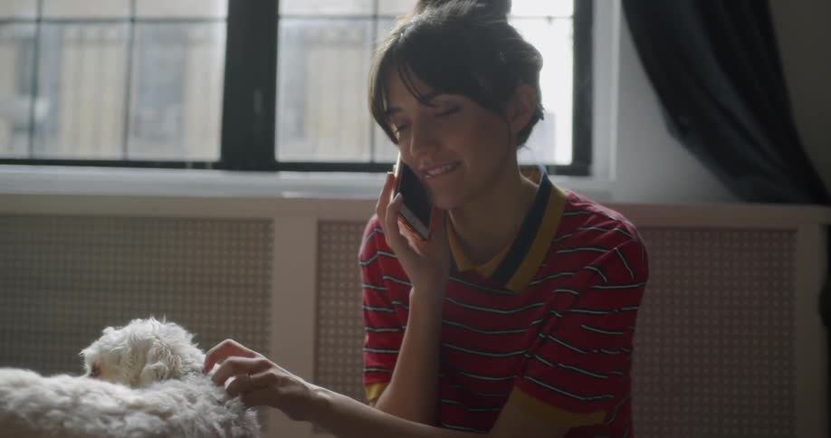 Woman pets a small white dog while talking on a phone