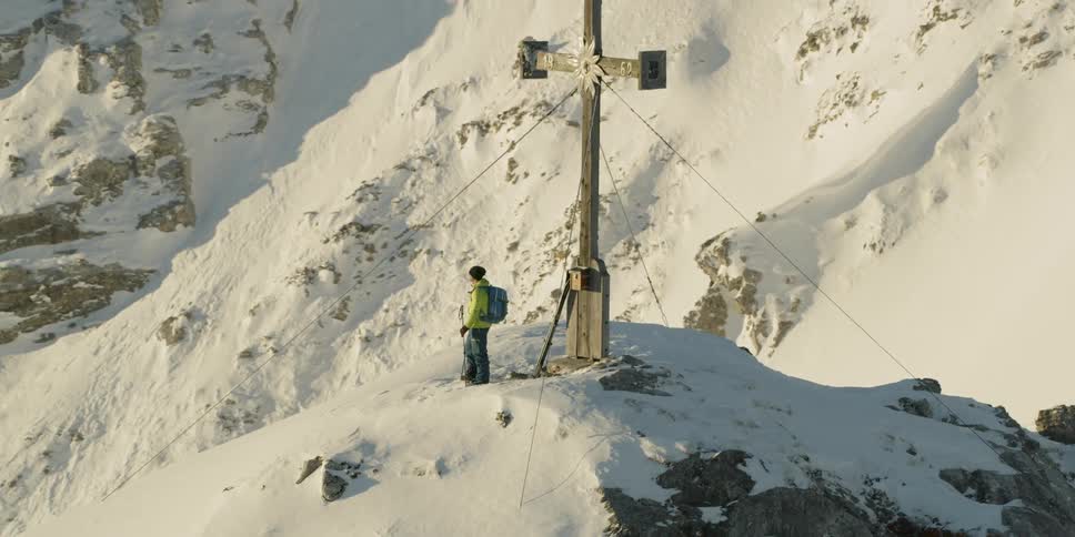 Man stands next to a large cross on a snowy mountain