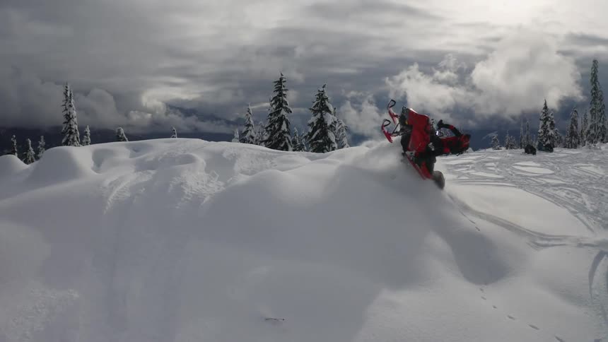 A person rides a snowmobile up a mound and turns mid air