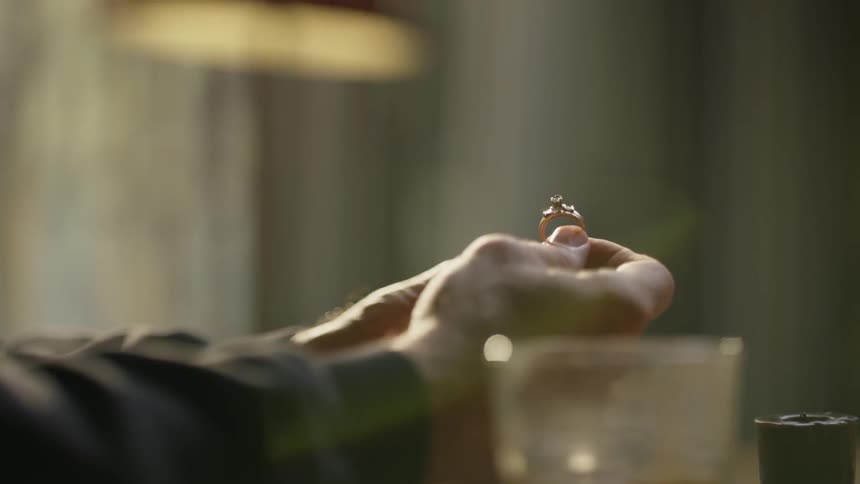 A man sits alone at a table holding a gold ring
