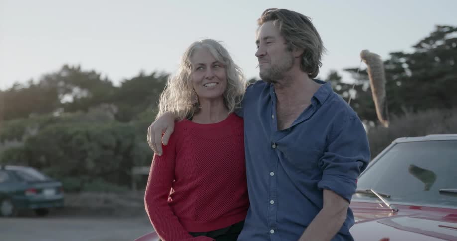 Man leans against a car with his arm around a woman