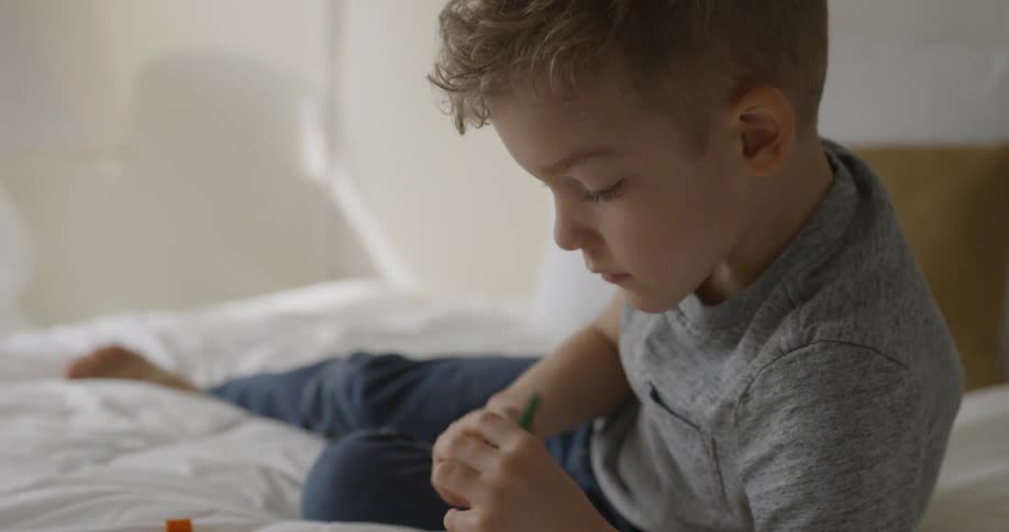 A young boy plays with legos on a bed