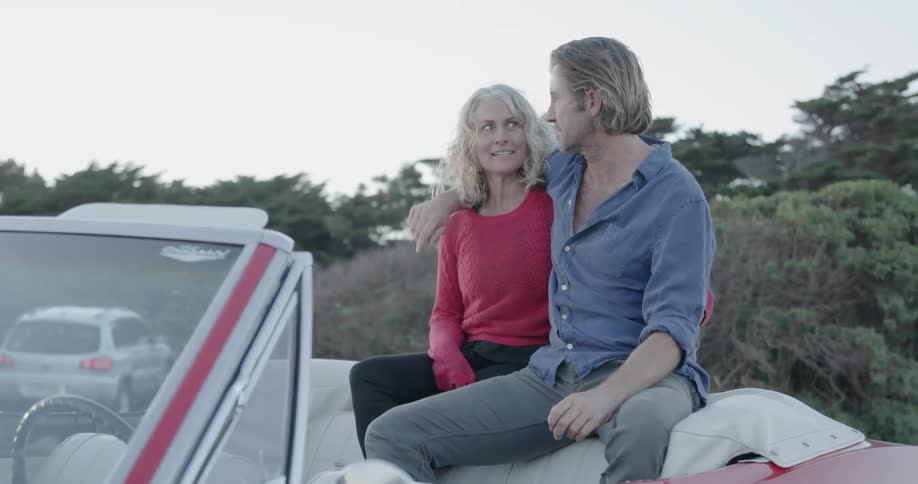 A couple are sharing a romantic moment as they are parked in a natural setting at sunset