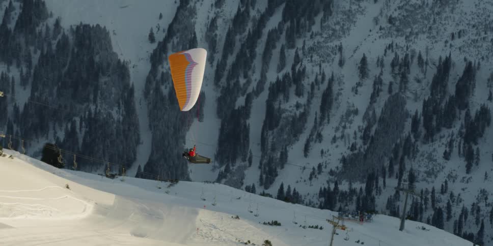 A person paraglides over snow covered mountain slopes