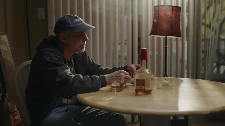 Man sits at a table near a bottle of alcohol