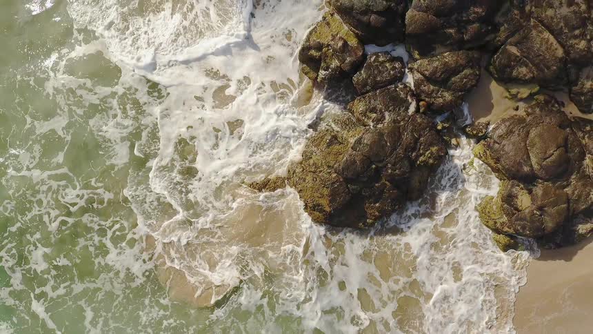 The rough waves crash against the rocks on a sunny day
