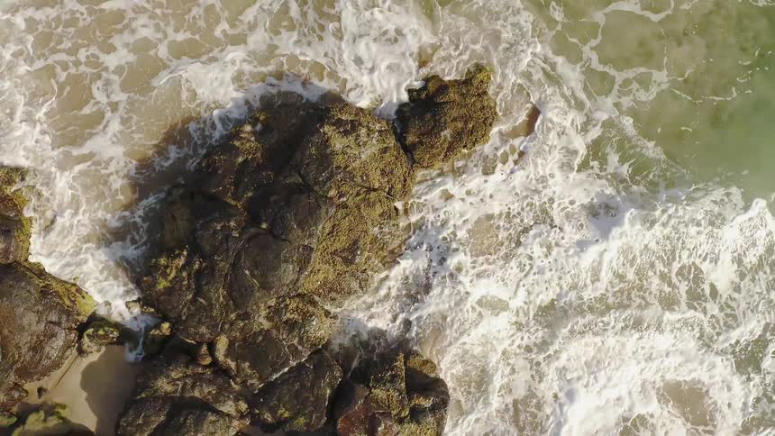 Waves are crashing against rocks on a beach during the day