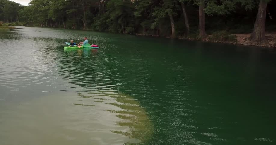 An adult and a child are fishing from canoes in a river during the day