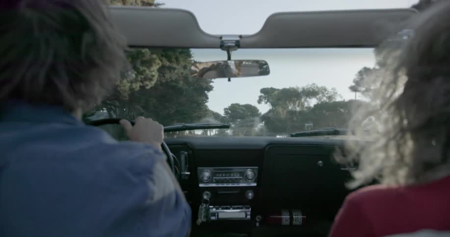 A man and woman travel in a convertible on a sunny day
