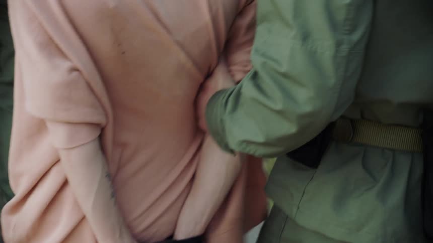 A prisoner has their hands tied behind their back with rope