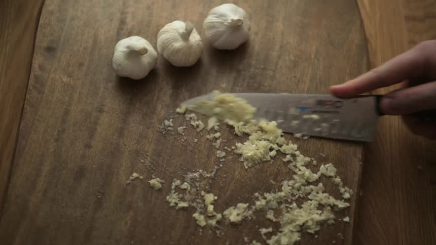 Someone is scraping up garlic with the back of a knife