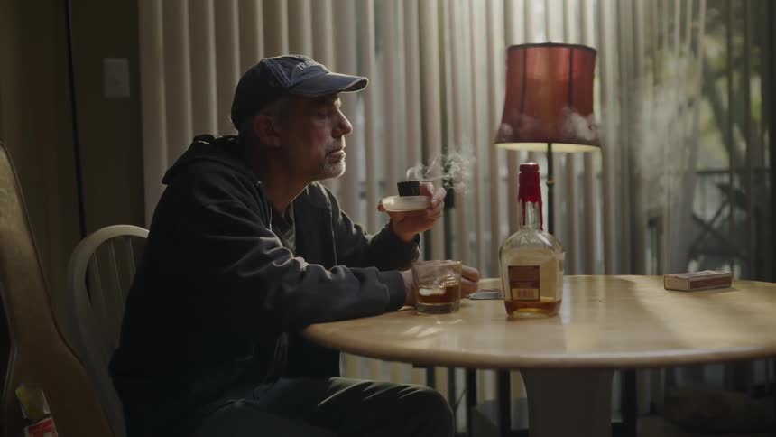 A man sitting at a table in his home is blowing out a candle
