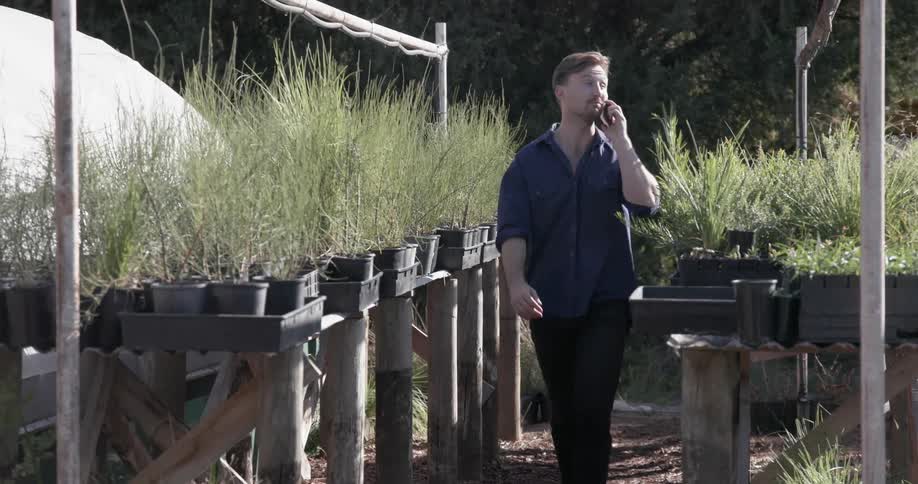 Smiling man walks through garden talking on a phone