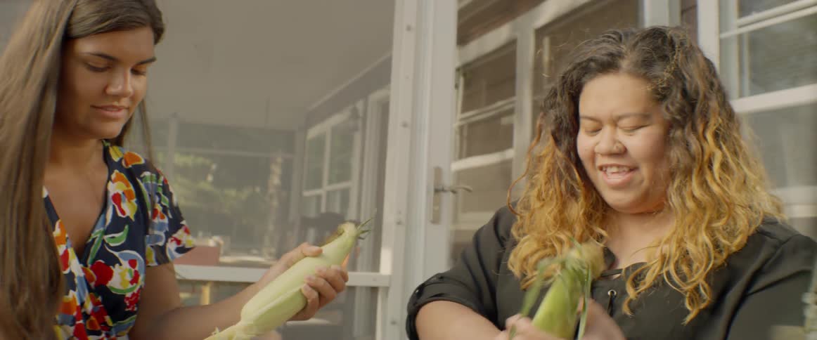 Two women shuck corn on the cob