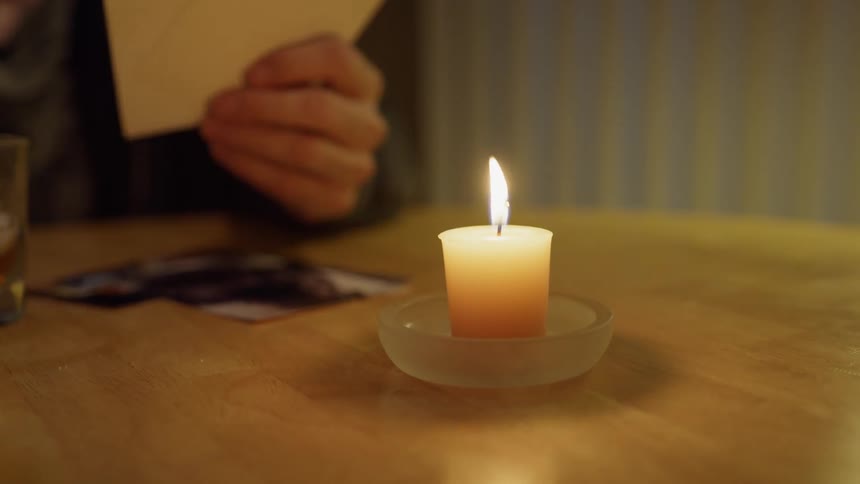 A man is looking at pictures at dusk as a candle burns on his dining room table