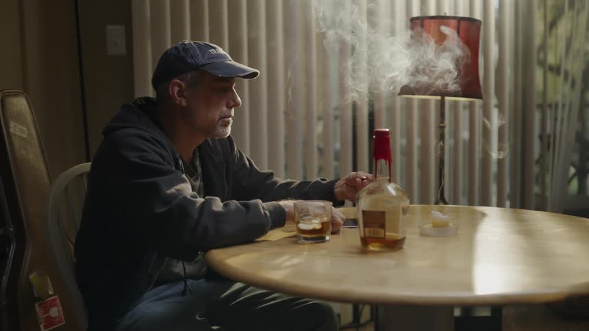 The man is smoking and drinking at the table