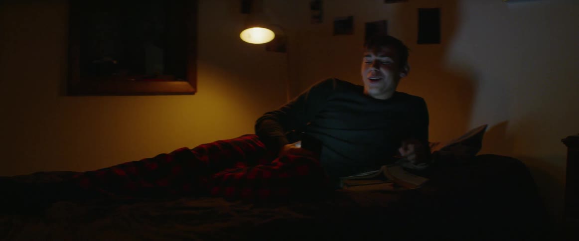 Boy lays on bed laughing and talking with someone on his tablet