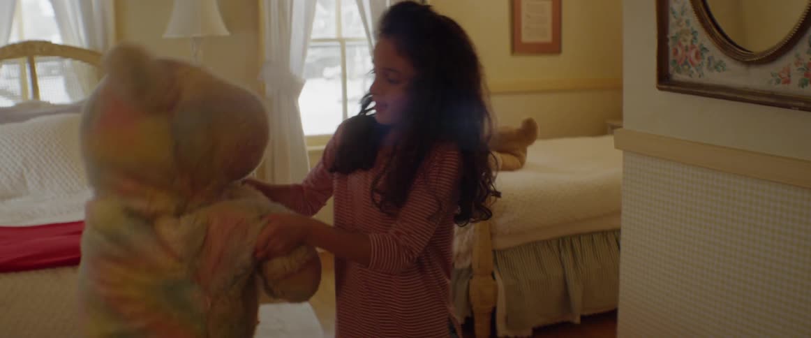 A girl plays with a large teddy bear in her room