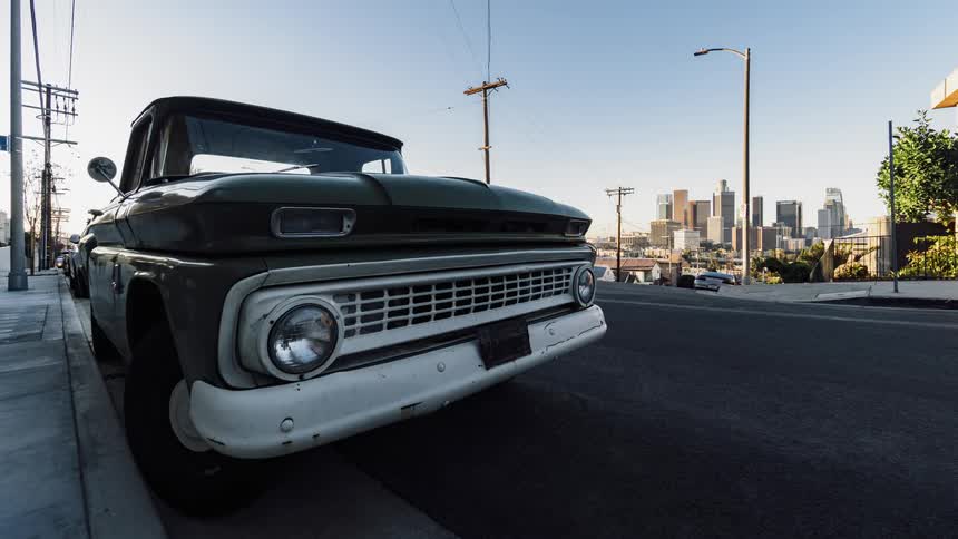 An old pickup truck is sitting on an urban street throughout the day
