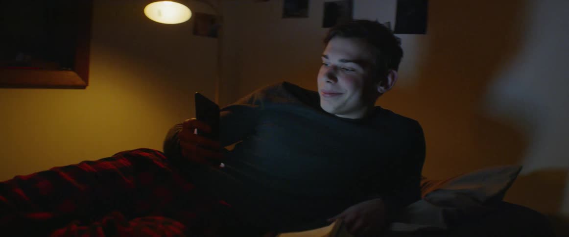 Boy sits in bed looking at his phone at night