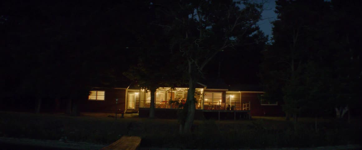 Group of people are sitting at table outside on porch at night