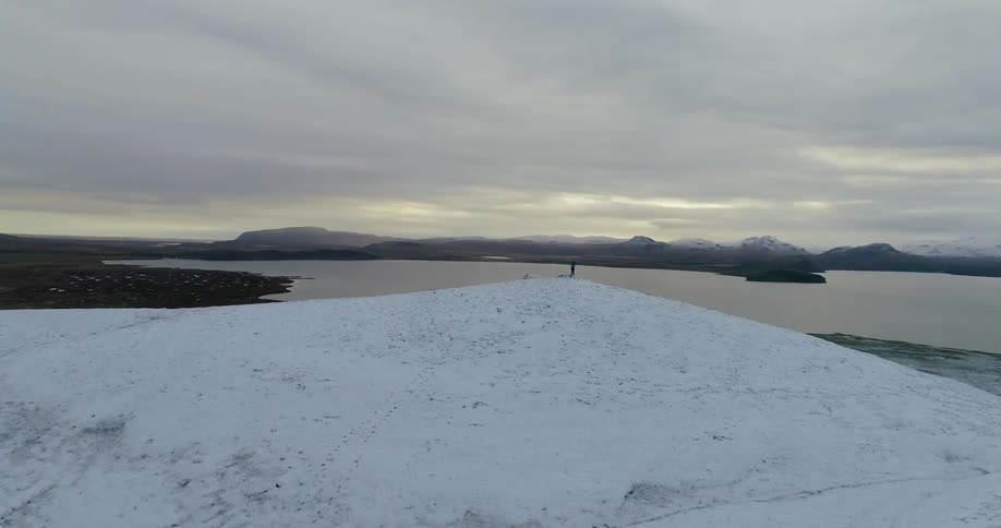 A hiker stands on a snowy mountain peak at sunset