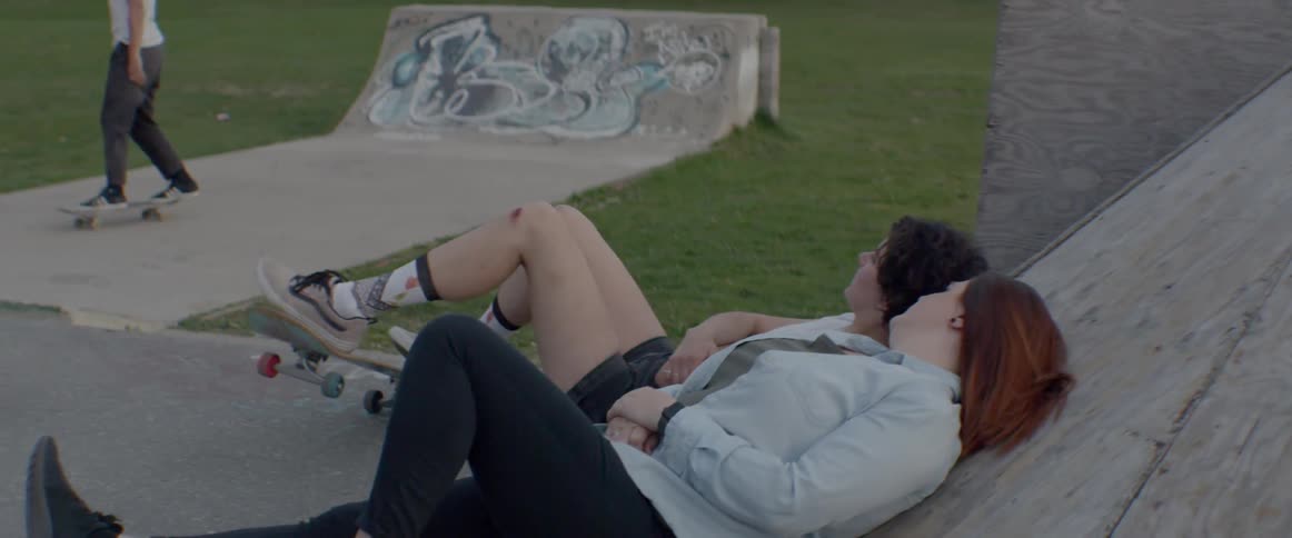 Girls lean back against a ramp while others skate in a skateboard park