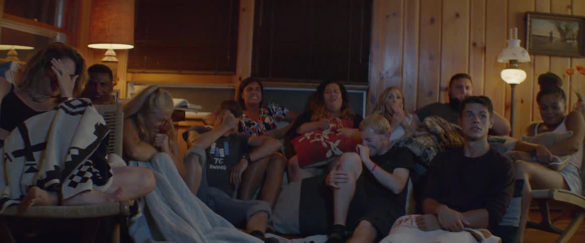Group of people sit on the floor and a sofa watching television