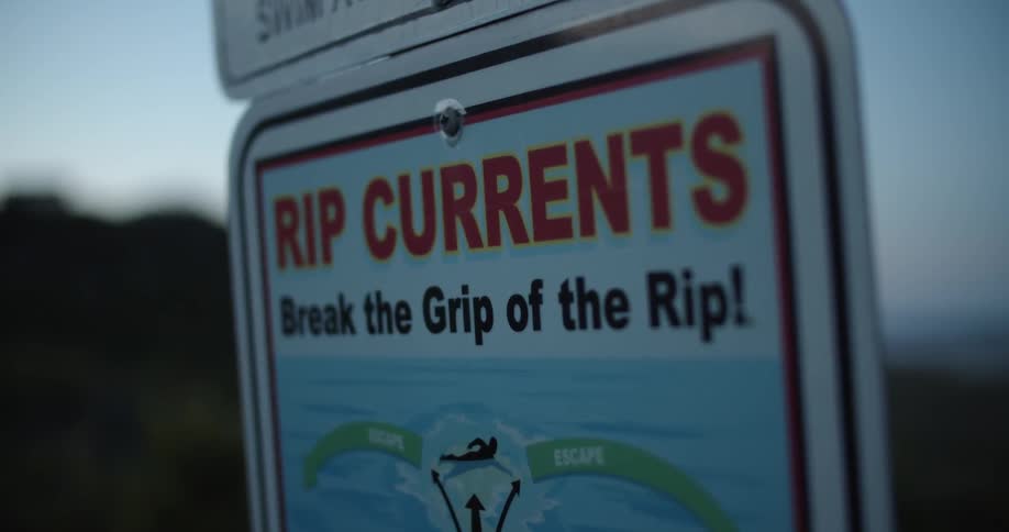 A sign warning of rip currents stands on a beach