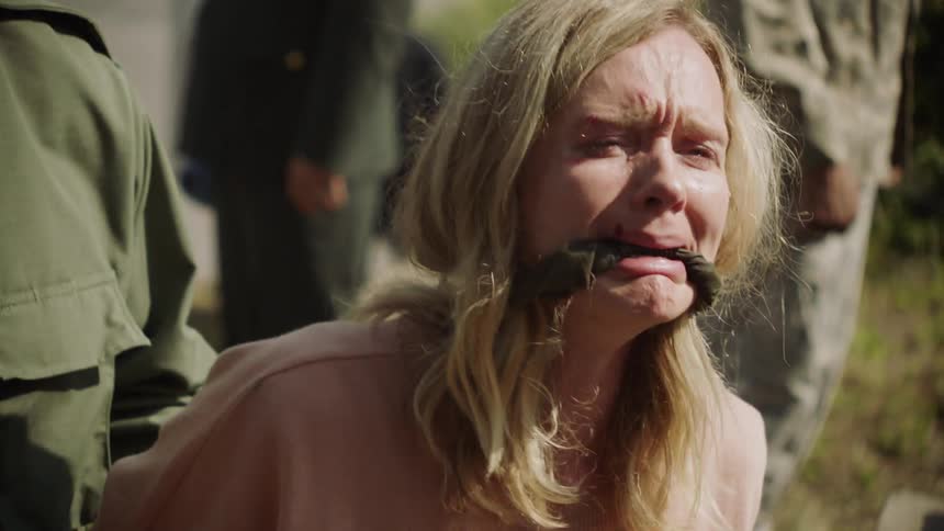 Solder stands behind a crying woman with a gag in her mouth