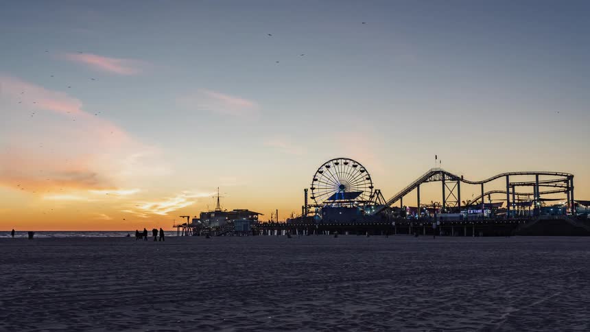 The sun sets over an amusement park on a beach